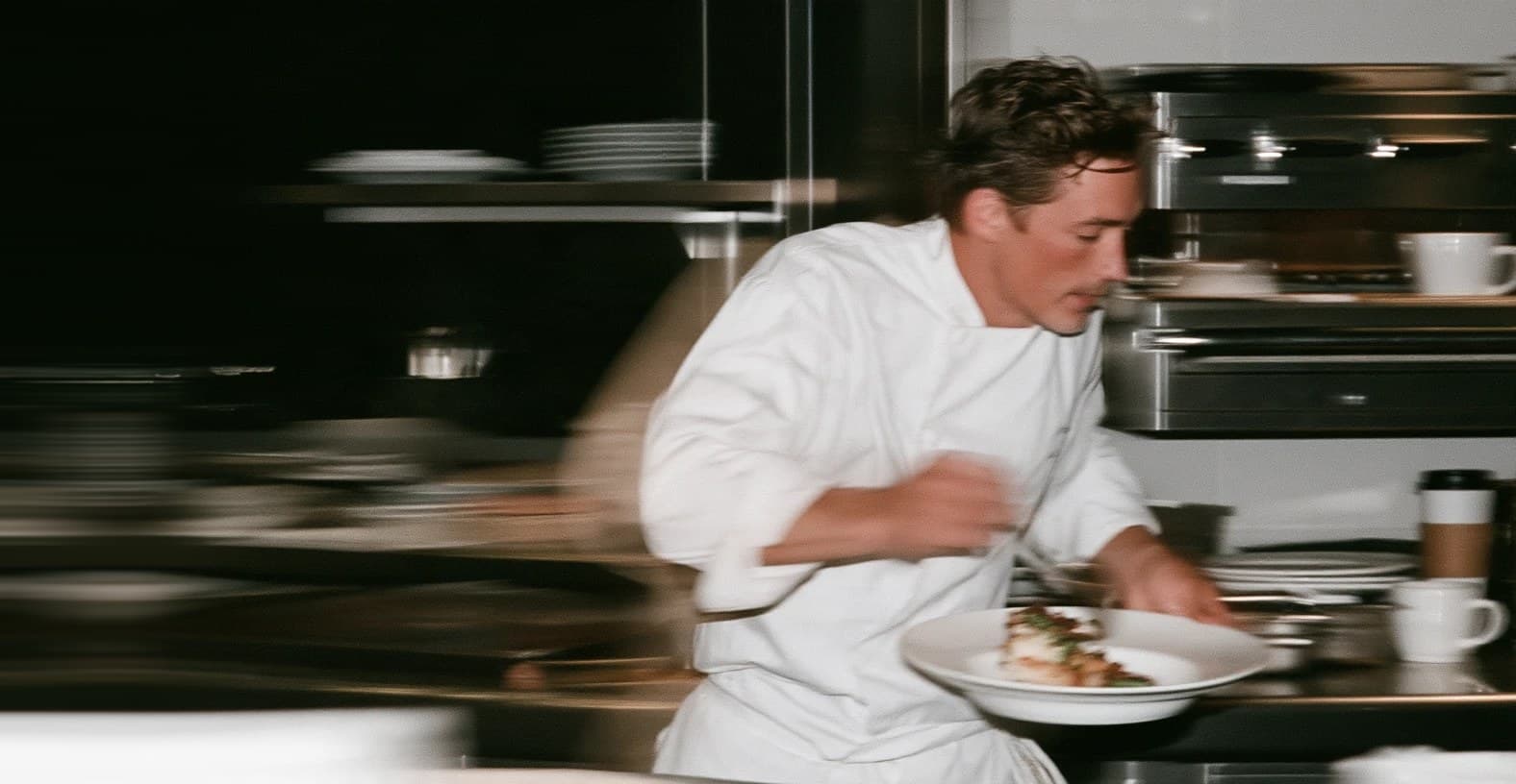 A chef hurries a plate across a busy kitchen